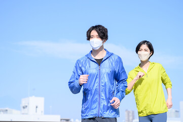 青い空で運動する健康的な男女　マスクつき
