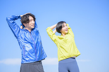青い空で準備運動する健康的な男女　横顔　広角