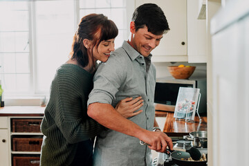 Food tastes best when made with love. Shot of a man cooking while being embraced by his wife at home.