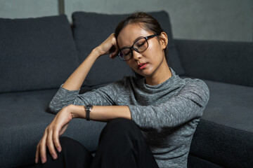 Obraz premium Young woman sitting with depression emotion on face, wear glasses, close eye, dark room, Portrait of young beautiful woman or female or girl sitting expression depression emotional alone