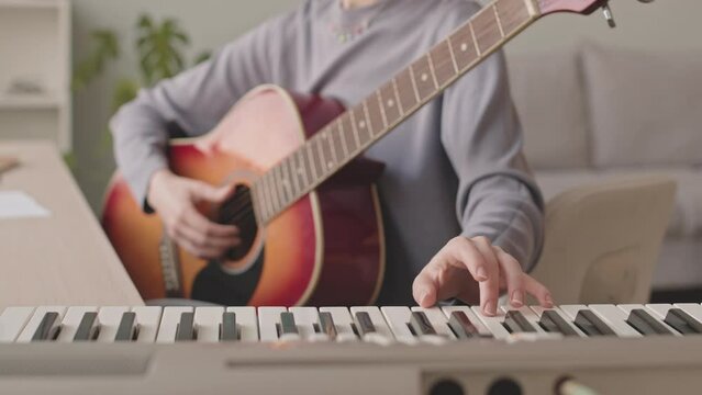 Cropped slowmo of unrecognizable female musician playing keyboard and guitar while practicing at home, writing new song