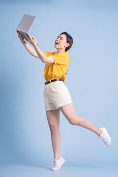 Full Length Image Of Young Asian Girl Using Laptop On Blue Background