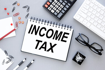 Income Tax text on a notebook with a spring on a gray background near the calculator