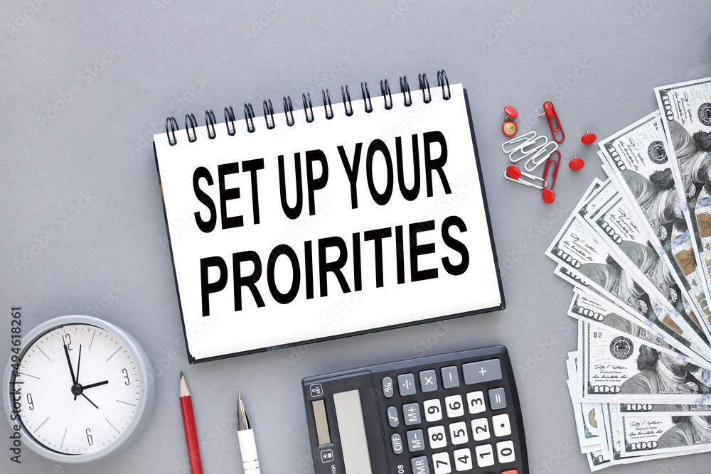Poster set up your priorities text on a notebook on a gray background against the background of dollar bill