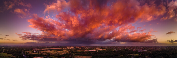 Firey storm clouds orange pink and red at sunset with distant rain storm across the landscape...
