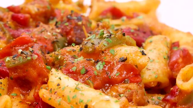 Detailed macro shot of spices on top of macaroni with red tomate sauce and vegetables. Rotating close up view of italian pasta in 4k.