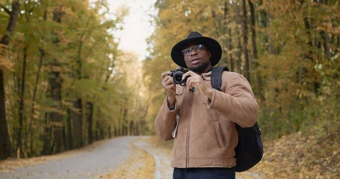 A black traveler with a camera takes pictures of the autumn forest
