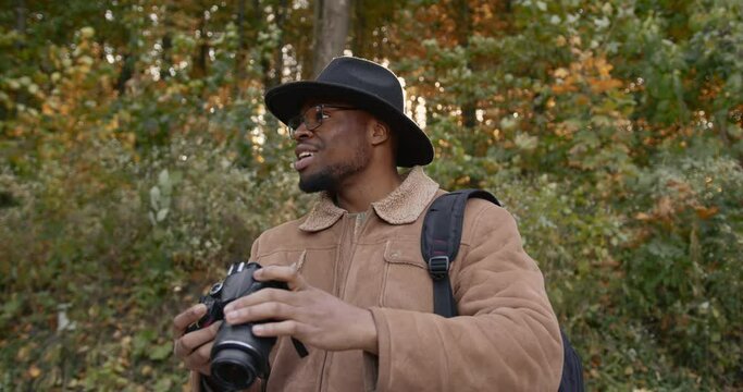 Black traveler with a camera in autumn forest