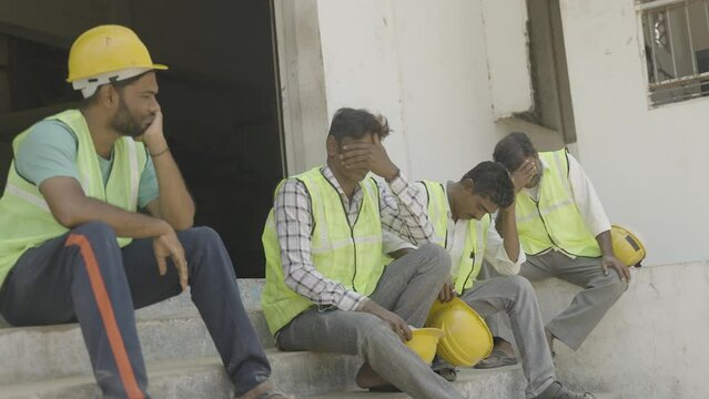 worried industrial workers sitting outside the factory due to closure - concept of job loss, unemployment and blue collar jobs