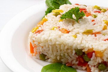 Cooked white rice mixed with colorful vegetables on white plate