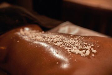 Woman back with salt during scrub in spa salon