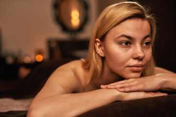 Thoughtful woman resting on massage table in spa