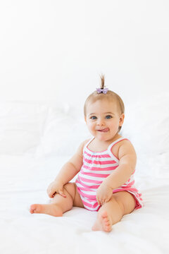 Funny baby girl sitting on white bed with tongue sticking out