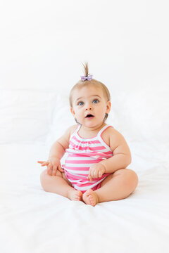 Cute chubby baby girl sitting on white bed