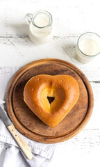 Milk bread in shape of the heart on wooden cutting board. Milk in jar and glass aside, grey napkin