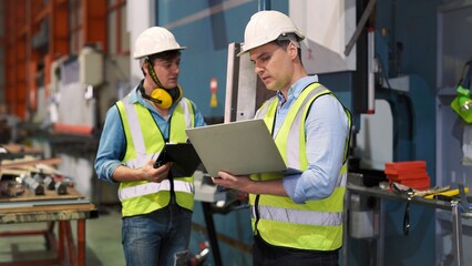 Two professional industrial engineer specialist with safety vast uniform and helmet holding laptop...