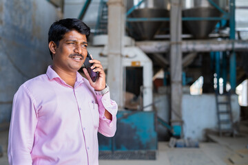 happy supervisor or manager busy talking on mobile phone while at factory - concept of taking...