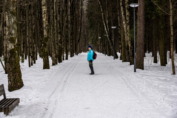 a woman in a blue jacket walks through a spring pine forest with the remains of snow 