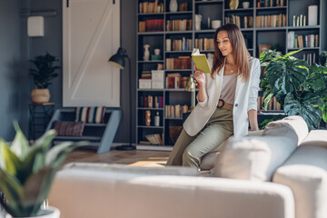 Woman sitting on couch and reading book . Relaxed businesswoman at home