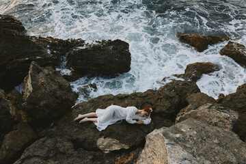 Beautiful bride lying on rocky coast with cracks on rocky surface unaltered