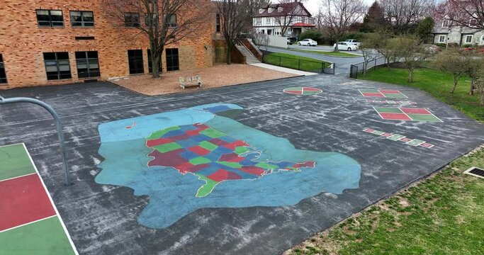 Aerial of school in community. View of playground at recess and approach USA map painted on asphalt driveway macadam pavement.