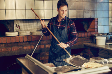 Master pizza maker at work. Shot of a young man using a peel while making a pizza behind the...