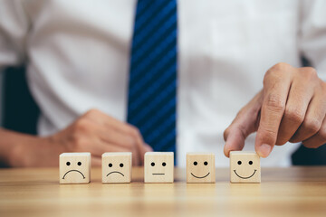 Closeup hands holding smiley face icon on wooden cube, service rating, leadership and corporate...