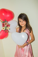 A girl wearing a pink dress fun amidst balloons.