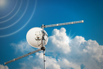 Close-up of a Satellite Dish and Television Aerial against a clear blue sky with clouds, sunbeams...