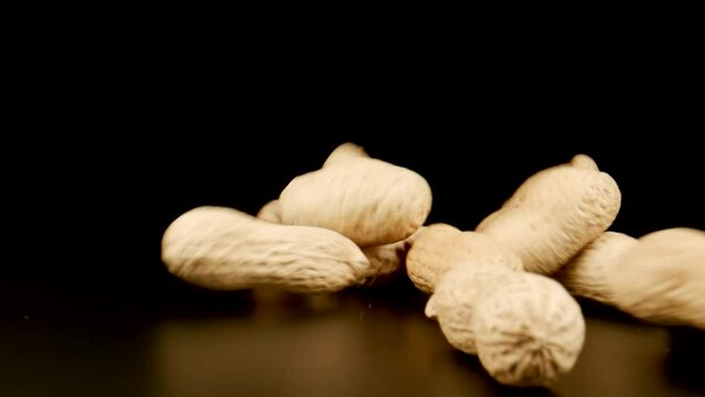 MACRO: Unpeeled peanuts fall on a black table, Slow motion