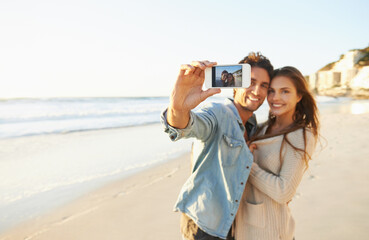 Love at the beach. Shot of an affectionate young couple taking a selfie at the beach.