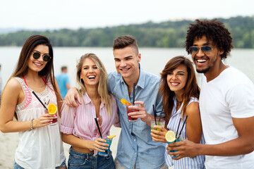 Happy young people, friends having fun on the beach and drinking cocktails together.