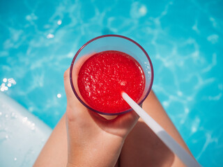 Beautiful glass with a refresh strawberry smoothie and a pretty woman on the background of the swim pool. Top view, close-up. Vacation and travel concept. Moments of celebration