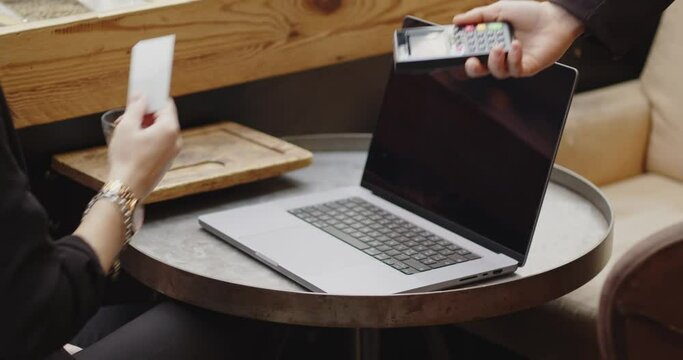 Close-up of a woman sitting in a cafe with laptop, paying with credit card.mart payment,contactless payment,e-money,digital money. Woman working,studying in a coffee shop