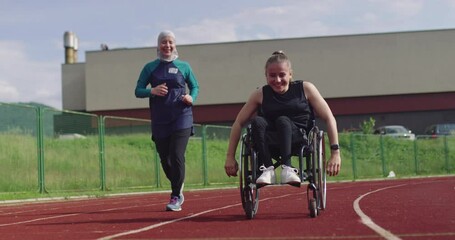A female person with disabilities riding a wheelchair on a athletics training track with muslim woman wearing hijab sportwear