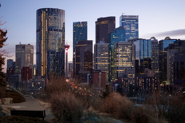 Calgary city at sunset with large buildings with lights on with the sun at sunset park near calgari tower in the background