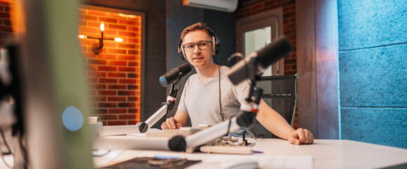 The DJ hosts the program and communicates with the audience on air at the radio station. The announcer reads the news. A male radio host speaks into a microphone and records a podcast