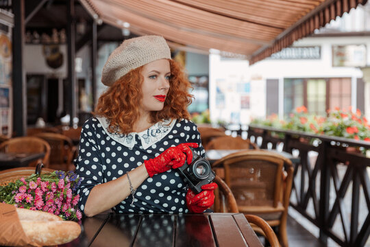 A woman in a beret and vintage dress holds a camera in her hands and takes shoots