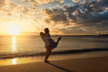 Fototapeta na wymiar A happy, hugging romantic holiday couple on a beach during golden sunset time