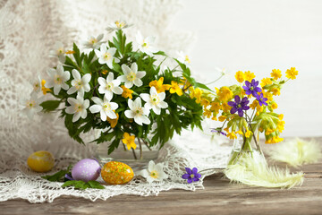 Easter still life with spring white, yellow and purple flowers in vases and egg decorations on the table