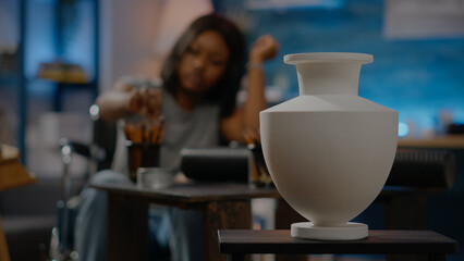 Close up of white vase ready for authentic drawing at art studio. Invalid african american artist in wheelchair working on masterpiece canvas using pencil and inspiration for project