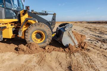 Bulldozer or loader moves the earth at the construction site against the blue sky. An earthmoving machine is leveling the site. Construction heavy equipment for earthworks.