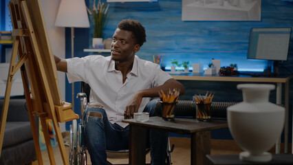 Young black person with disability designing vase drawing on canvas in workshop space. Disabled african american artist in wheelchair working on beautiful masterpiece for fine art