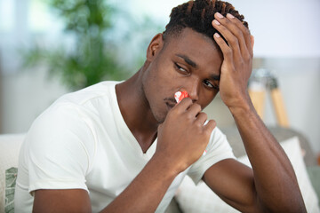 young man with tissue in his nostril has nose bleed