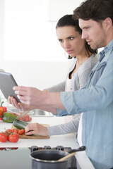 happy couple following recipe on digital tablet when cooking