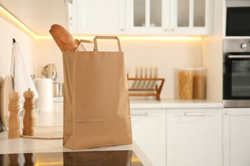 Obraz na płótnie Canvas Paper shopping bag with baguette on white countertop in kitchen. Space for text