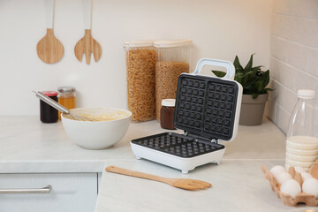 Modern electric waffle maker and ingredients on white countertop indoors