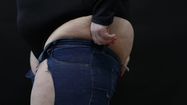 fat woman with cellulite trying to put on jeans on black background