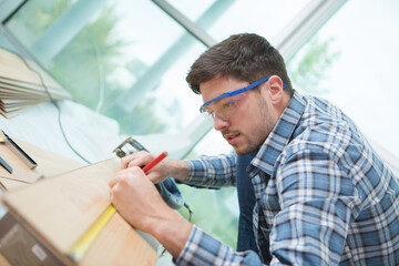 Naklejka na ściany i meble man measuring wooden planks with tape and pencil