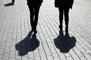 Silhouettes and shadows of two women walking down the street. Concept of female friendship,...